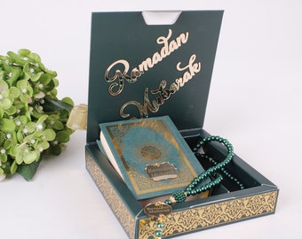 Könnte beinhalten: Eine grüne Geschenkbox mit goldenen Akzenten und einem komplizierten Design. Die Box ist geöffnet und enthält ein grünes Buch mit goldenen Lettern, auf dem "Ramadan Mubarak" steht, und eine grüne Gebetskette.