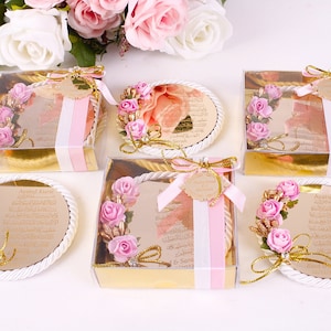 Peut inclure: Cinq petites bo&icirc;tes transparentes avec des bordures dor&eacute;es contiennent des plaques rondes, blanches et d&eacute;coratives avec une bordure en corde dor&eacute;e. Chaque plaque pr&eacute;sente un motif floral rose et du texte arabe. Le texte sur une plaque indique "Ayatul Kursi".