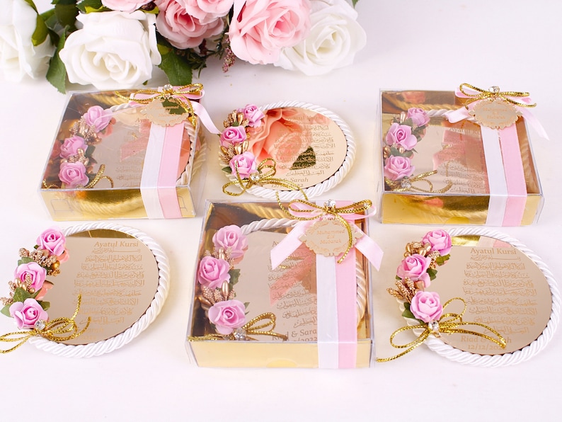 Peut inclure: Cinq petites bo&icirc;tes transparentes avec des bordures dor&eacute;es contiennent des plaques rondes, blanches et d&eacute;coratives avec une bordure en corde dor&eacute;e. Chaque plaque pr&eacute;sente un motif floral rose et du texte arabe. Le texte sur une plaque indique "Ayatul Kursi".