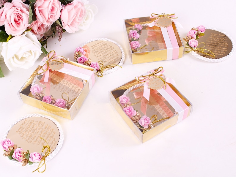 Peut inclure: Quatre petites bo&icirc;tes cadeaux avec des couvercles transparents et des finitions dor&eacute;es. Chaque bo&icirc;te contient un miroir rond, blanc et d&eacute;coratif avec des fleurs roses et des accents dor&eacute;s. Les miroirs portent du texte arabe. Les bo&icirc;tes sont attach&eacute;es avec un ruban rose et blanc.