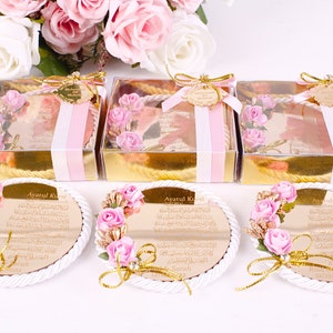 Peut inclure: Trois bo&icirc;tes dor&eacute;es avec un ruban rose et blanc, chacune contenant un petit miroir rond avec un cadre dor&eacute; et des fleurs roses. Les miroirs portent l'inscription "Ayatul Kursi" en lettres dor&eacute;es.