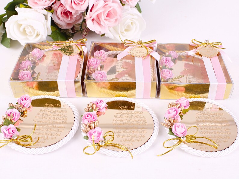 Peut inclure: Trois bo&icirc;tes dor&eacute;es avec un ruban rose et blanc, chacune contenant un petit miroir rond avec un cadre dor&eacute; et des fleurs roses. Les miroirs portent l'inscription "Ayatul Kursi" en lettres dor&eacute;es.