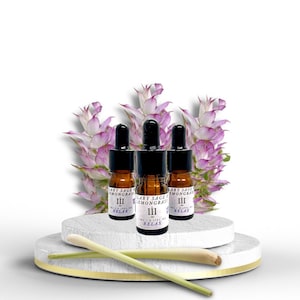 May include: Three small brown glass bottles with black droppers and labels that read "Clary Sage & Lemongrass III RELAX" are arranged on a white marble platform. Two green stalks of lemongrass are on the platform.