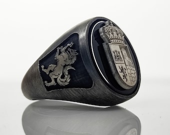 May include: A silver ring with a black enamel inlay featuring a coat of arms with a wolf, a crown, and a building. The ring is on a white background.