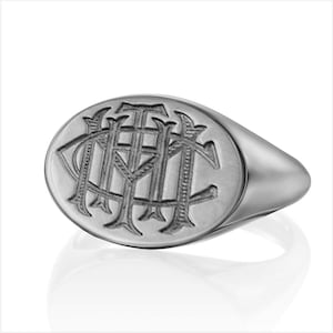 May include: A silver signet ring with an oval-shaped top featuring an engraved monogram.