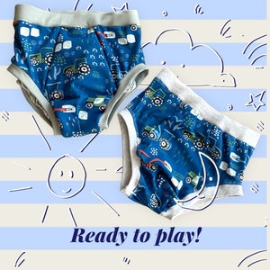 May include: Two pairs of blue and grey toddler underwear with a tractor print. The underwear has a grey waistband and a white crescent moon on one pair.