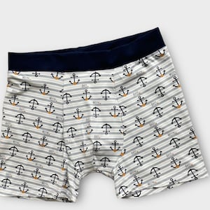 Könnte beinhalten: Boxershorts mit weiß-grauen Streifen und einem marineblauen Bund. Die Shorts sind mit schwarzen Ankern und den Wörtern "MOIN" und "AHOI" im maritimen Stil bedruckt.