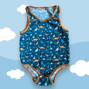 May include: A sleeveless bodysuit in a deep teal color featuring a repeating pattern of various dinosaurs in shades of orange, white, and light blue. The garment is finished with solid brown trim around the neckline, armholes, and leg openings.