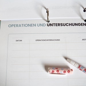 May include: A white notebook with a black header that reads "Operationen und Untersuchungen". The notebook has columns labeled "Datum", "Operation/Untersuchung", and "Arzt". A pen with a floral pattern is lying on the notebook.