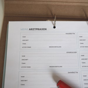May include: A white binder with a blue border and the text "Meine Arztpraxen" at the top. The binder has sections for different types of doctors, including a general practitioner, gynecologist, and dentist. Each section has fields for the doctor's name, address, email, and last appointment.