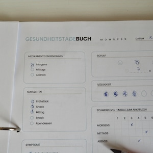May include: A health journal with the title "GESUNDHEITSTAGEBUCH" in German. The journal includes sections for medication, meals, sleep, and pain levels. The date 22.7.22 is handwritten at the top. The journal is open to a page with check marks.