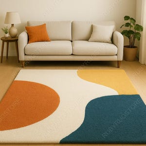 May include: A modern area rug with an abstract design. The rug features large, curved shapes in orange, cream, yellow, and teal. The rug is placed on a hardwood floor in front of a beige sofa.
