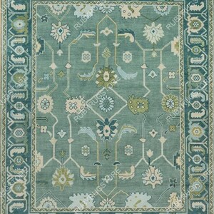 May include: A teal blue rug with a geometric pattern featuring floral motifs. The rug has a border with a repeating design of stylized leaves and flowers.