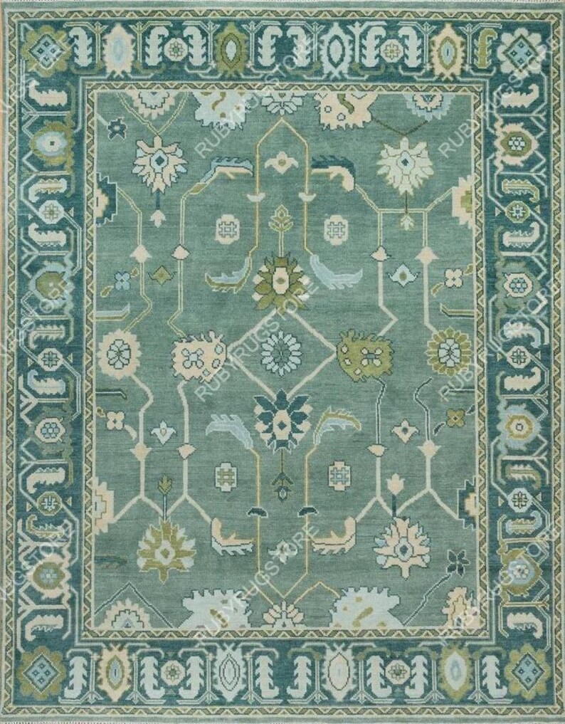 May include: A teal blue rug with a geometric pattern featuring floral motifs. The rug has a border with a repeating design of stylized leaves and flowers.