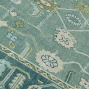 May include: A teal blue rug with a geometric pattern featuring green, white, and pink accents. The rug has a traditional design with intricate details.
