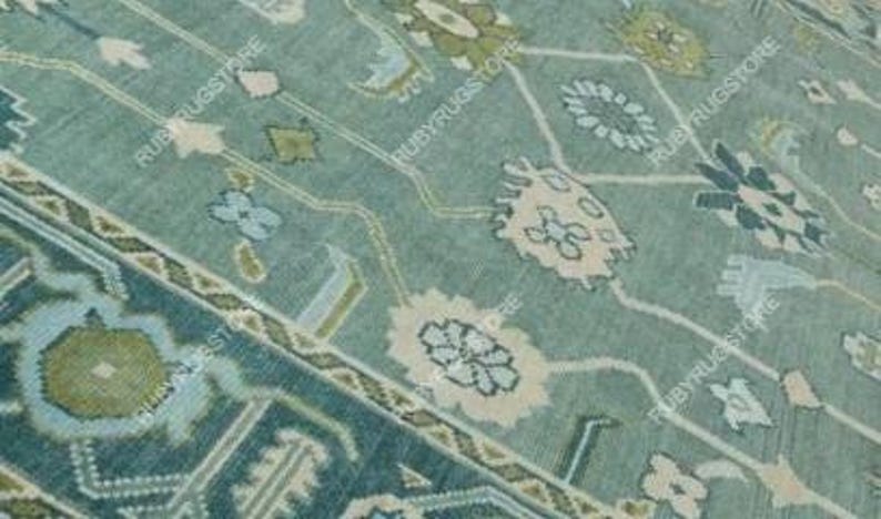 May include: A teal blue rug with a geometric pattern featuring green, white, and pink accents. The rug has a traditional design with intricate details.