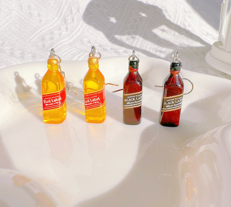 May include: Miniature bottle earrings. Two yellow bottles with red labels that read "Red Label" and two brown bottles with black labels that read "Black Label". The earrings have silver-colored hooks.