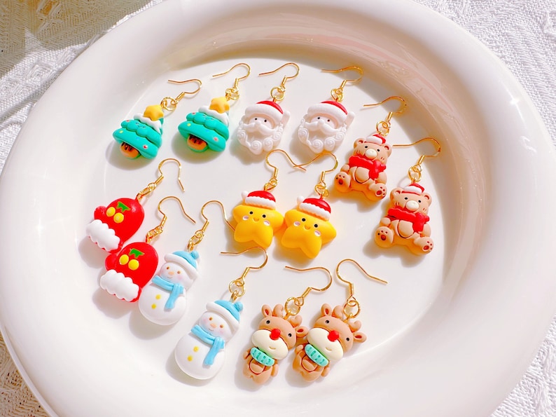 May include: A collection of Christmas-themed dangle earrings. Designs include Christmas trees, Santa Claus, teddy bears, mittens, snowmen, star-shaped ornaments, and reindeer. Each earring has a gold-colored hook.