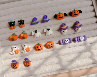 May include: A collection of Halloween-themed earrings, including black cats, witch hats, pumpkins, ghosts, skull-wearing witch hats, and candy. The earrings are in various colors, including orange, purple, black, and white. The earrings are displayed on a beige jewelry tray.