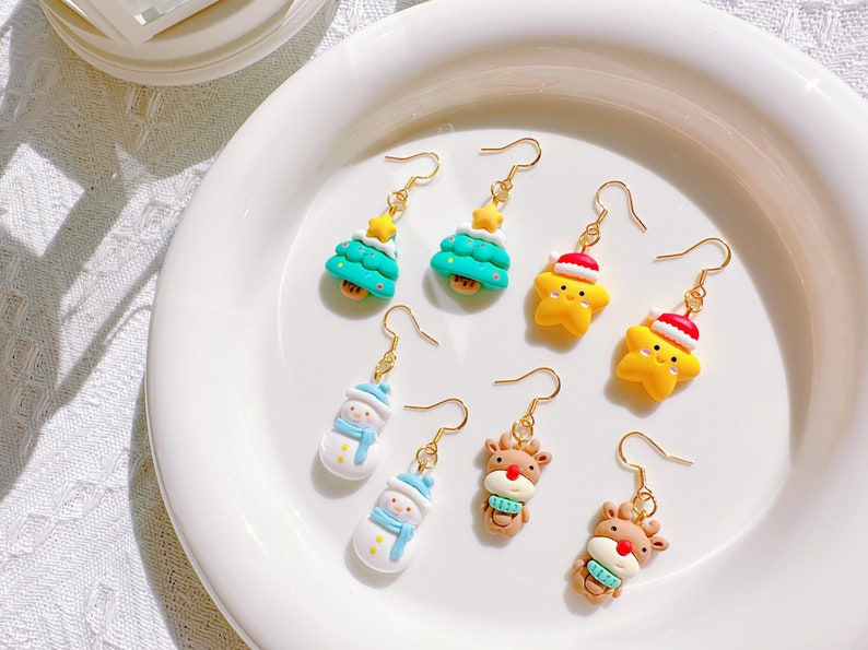 May include: A collection of Christmas-themed dangle earrings. The earrings feature designs of Christmas trees, snowmen, stars wearing Santa hats, and reindeer. Each earring has a gold-colored hook.