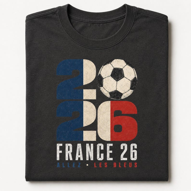 May include: A charcoal grey t-shirt featuring a graphic with the number 2026, where the zero is replaced by a black and white football. The design incorporates blue, white, and red colours, with the text FRANCE 26 and ALLEZ LES BLEUS below.