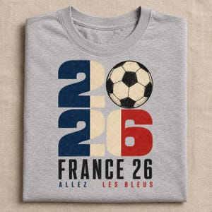 May include: A heather grey t-shirt featuring a large graphic of the number 2026, with the zero replaced by a black and white football. The design incorporates the colours of the French flag, with the text FRANCE 26 and ALLEZ LES BLEUS below.