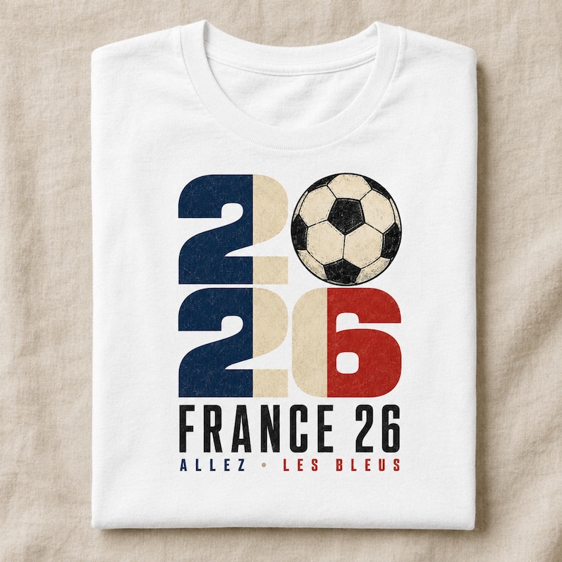 May include: A white t-shirt featuring a graphic with the number 2026, where the zero is replaced by a black and white football. The design incorporates blue, white, and red colours, with the text FRANCE 26 and ALLEZ LES BLEUS printed below.