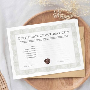 Op de afbeelding: Een wit certificaat van echtheid met een decoratieve rand. De tekst "CERTIFICATE OF AUTHENTICITY" staat bovenaan het document gedrukt. Het document bevat velden voor de kunstenaar, de titel van het kunstwerk, de afmetingen van het kunstwerk, de gebruikte materialen, het origineel of de print en de datum van productie. Een waszegel bevindt zich in de rechterbenedenhoek.