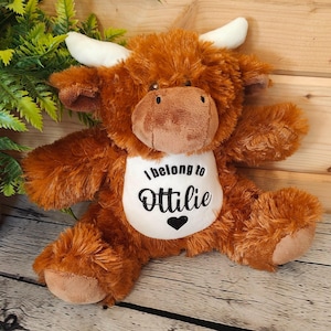 May include: Brown and white plush Highland cow stuffed animal with a white bib that says "I belong to Ottilie" with a black heart.