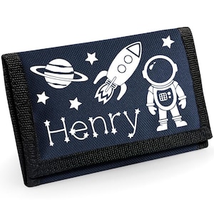 Peut inclure: Portefeuille bleu marine avec une fusée blanche, une planète, des étoiles et un astronaute. Le nom "Henry" est imprimé en blanc. Le portefeuille a une bordure noire et une fermeture velcro.