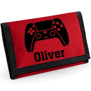 May include: Red wallet featuring a black controller design and the name "Oliver". The wallet has a black trim and a velcro fastening. The design is printed in black and is centered on the front.