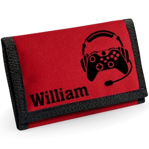 Puede incluir: Cartera roja con ribete negro y un gráfico negro de un mando de videojuegos y auriculares. El nombre "William" está impreso en negro. La cartera está hecha de tela duradera.