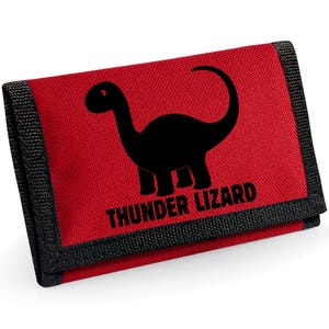 May include: Red trifold wallet with a black dinosaur silhouette and the text "THUNDER LIZARD". The wallet has black trim and a velcro closure. The design is centered on the front of the wallet.