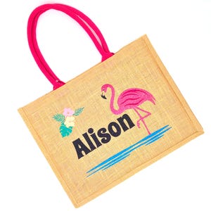 Natural colour jute bag with pink handle. Displays a pink flamingo using glitter htv, standing in a glitter blue lake, with flowers to one side, personalised with flamingorgeous in a black glitter font.