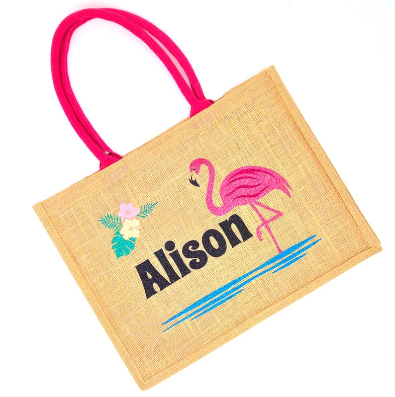 Natural colour jute bag with pink handle. Displays a pink flamingo using glitter htv, standing in a glitter blue lake, with flowers to one side, personalised with flamingorgeous in a black glitter font.