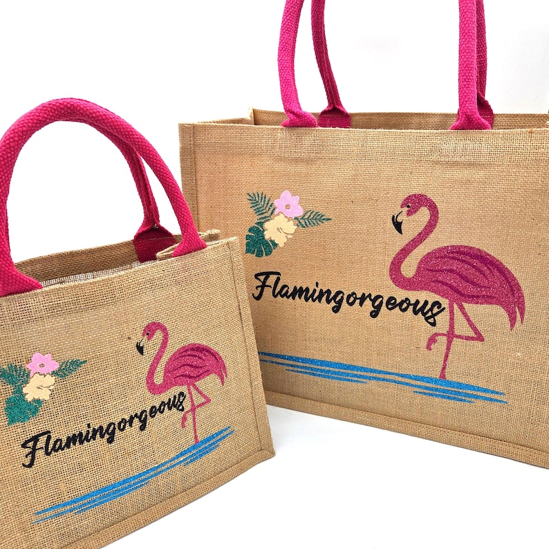 Natural colour jute bag with pink handle. Displays a pink flamingo using glitter htv, standing in a glitter blue lake, with flowers to one side, personalised with flamingorgeous in a black glitter font.