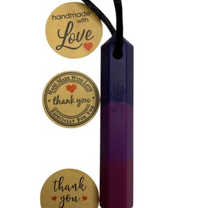 May include: A purple and blue pendant necklace with a black cord. The pendant is a geometric shape with a color gradient. The image includes three round tags with text that reads "handmade with love", "thank you", and "for supporting our small business".
