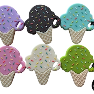 Op de afbeelding: Zes ijsje-hangers in paars, donkerbruin, lichtblauw, roze, wit en groen. Elke hanger heeft een gestructureerde wafelbasis en een bolletje ijs met veelkleurige hagelslag. Er zijn zwarte koorden aan de hangers bevestigd.