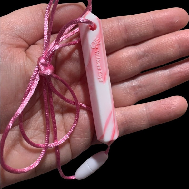 May include: A pink and white marble-patterned pendant necklace with the text "Willows Toys". The pendant is rectangular and attached to a pink cord with a breakaway clasp. The necklace is designed for babies and toddlers.