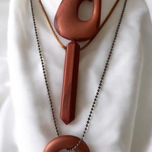 May include: Three necklaces with copper-colored pendants. The top necklace has a large, irregular pendant with a hole. The middle necklace has a long, rectangular pendant. The bottom necklace has a circular pendant.