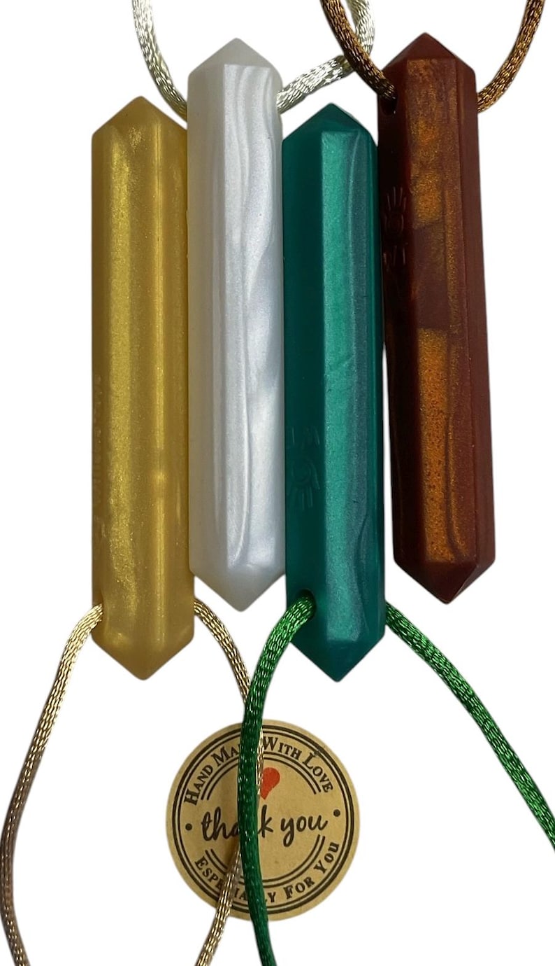 May include: Four gemstone pendants in gold, white, teal, and brown, each with a faceted, elongated shape. The pendants are suspended from cords of varying colors. A small tag with the words "thank you" is attached.
