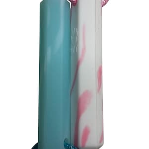 May include: Two hexagonal pendants, one light blue and one white with pink accents, are suspended on pink and teal cords. The pendants are connected and appear to be made of a smooth, solid material.