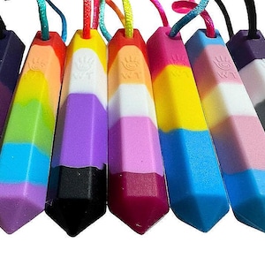 May include: A collection of colorful, prism-shaped pendants with cords. Each pendant features a different color scheme, including rainbow, pink, blue, and black, representing various pride flags. The pendants have a smooth, glossy finish.