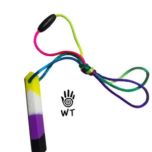 May include: A non-binary pride flag pendant necklace. The pendant is a rectangular prism with yellow, white, purple, and black sections. The necklace cord is a rainbow of colors, including pink, green, blue, and purple. The text "WT" and a hand symbol are on the right.