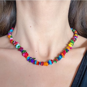 May include: A colourful necklace made of small, irregular shaped beads in shades of red, orange, yellow, green, blue, and purple.