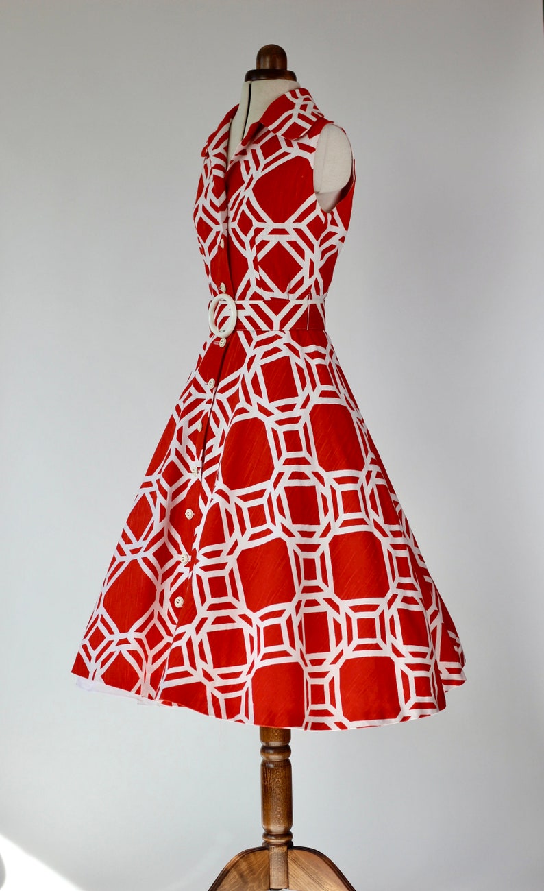 May include: A red sleeveless dress with a white geometric pattern and a white belt. The dress has a collared neckline and a button-up front.