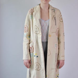 Peut inclure: Un long manteau crème avec un col et une fermeture à bouton. Le manteau est décoré de broderies colorées et de paillettes en forme de cercle.