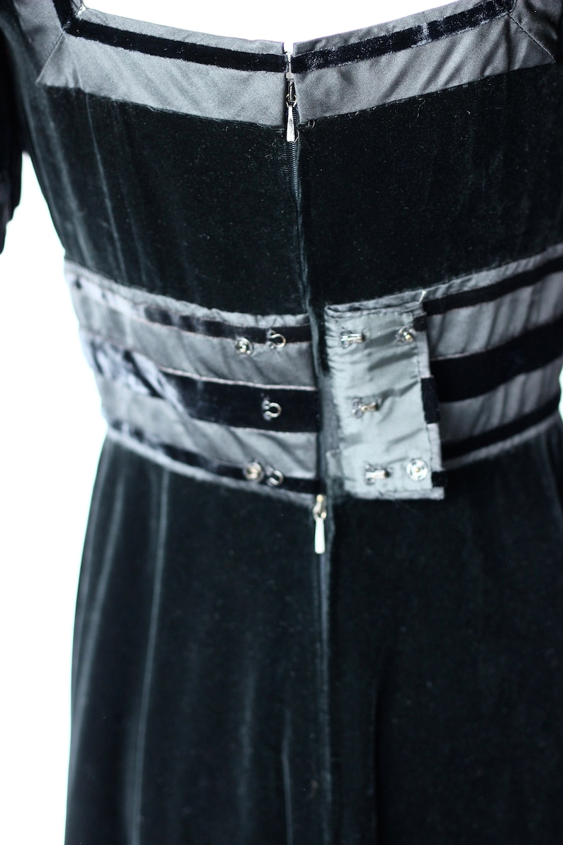 May include: Black velvet dress with a zip fastening and a black satin waistband with a row of buttons.