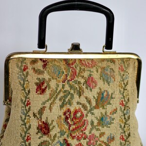 May include: Vintage handbag with a black handle and gold-toned frame. The beige fabric is intricately embroidered with a floral pattern in shades of red, pink, blue, and green. The bag has a classic, structured design.