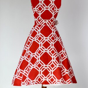 May include: A red and white sleeveless dress with a geometric pattern. The dress has a fitted bodice and a full skirt. The dress is on a mannequin.